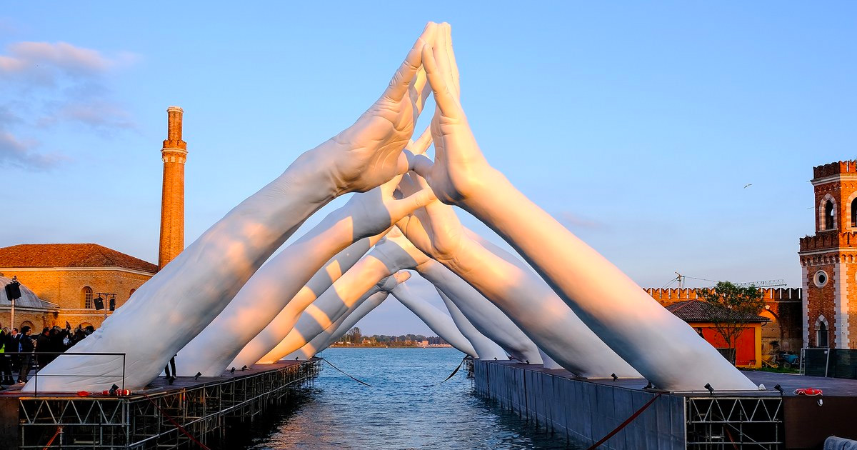 Instalação escultural com 6 pares de braços dando as mãos emerge dos canais de Veneza